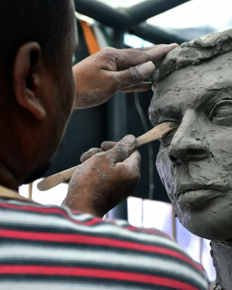 Detalle de unas manos modelando con esteca la zona del ojo en un retrato de barro